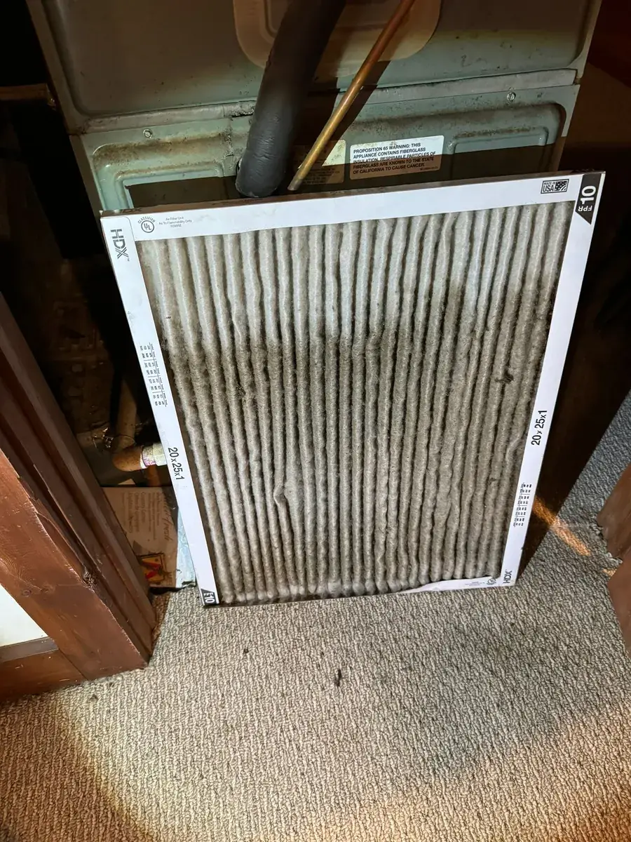 Heavily loaded HVAC filter caked with grey dust, found during a duct cleaning inspection